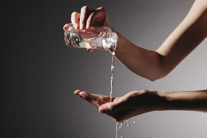 Person pouring water from a bottle into their hand against a dark background