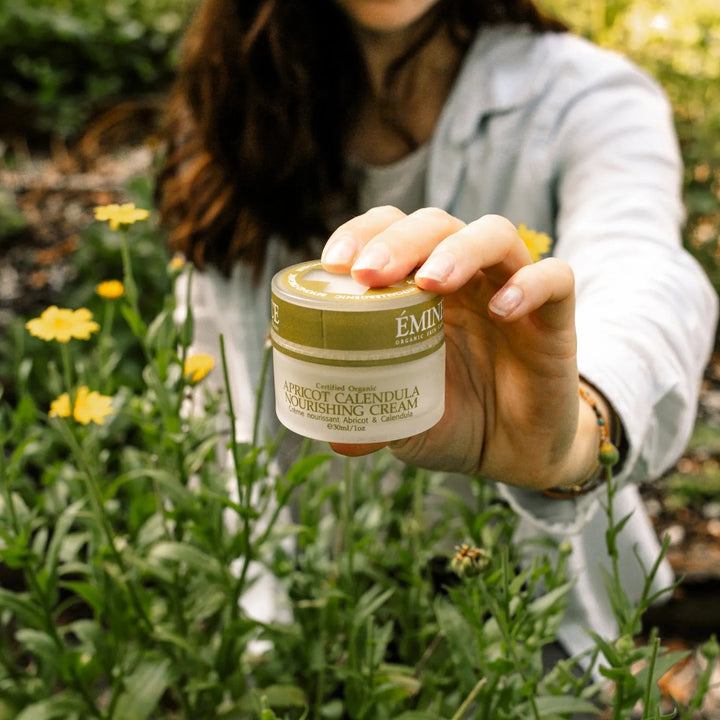 Person holding a jar of Eminence cream in a garden setting