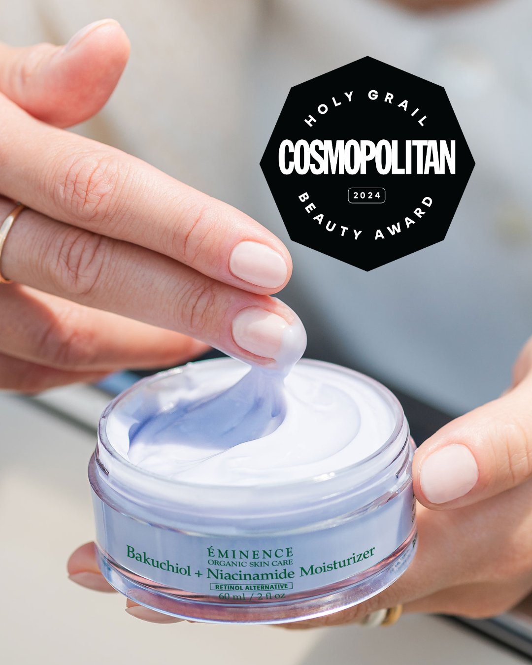 A hand lifting lavender-coloured Éminence Bakuchiol + Niacinamide Moisturizer from its jar