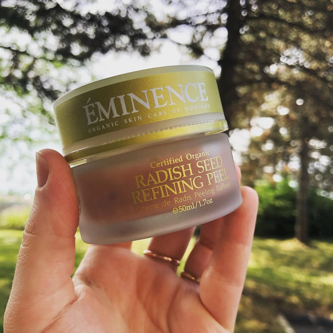 Hand holding a jar of Eminence Radish Seed Refining Peel against a blurred natural background